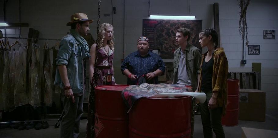 A group of people standing around three red barrels covered with some paper. 