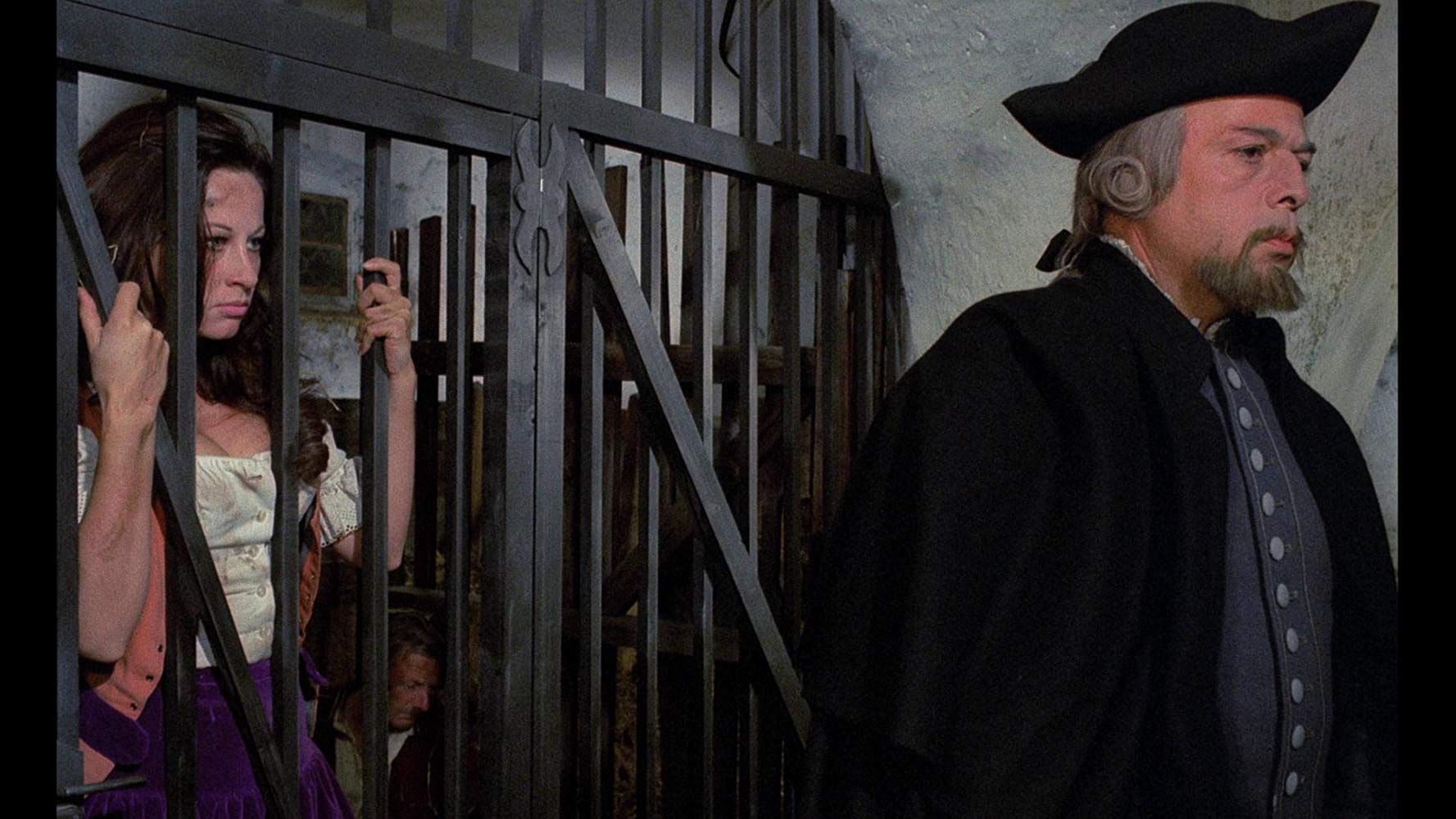 A young woman (Olivera Katarina) behind bars looking at an older man (Herbert Lom) with his back turned to her.