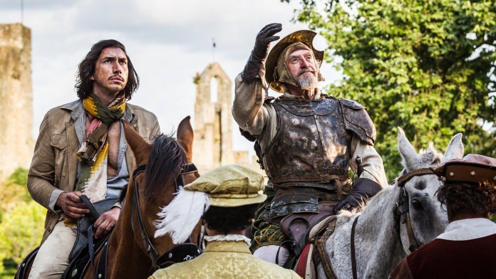 A younger man (Adam Driver) with a scarf and an older man (Jonathan Pryce) wearing a suit of armor on two horses.