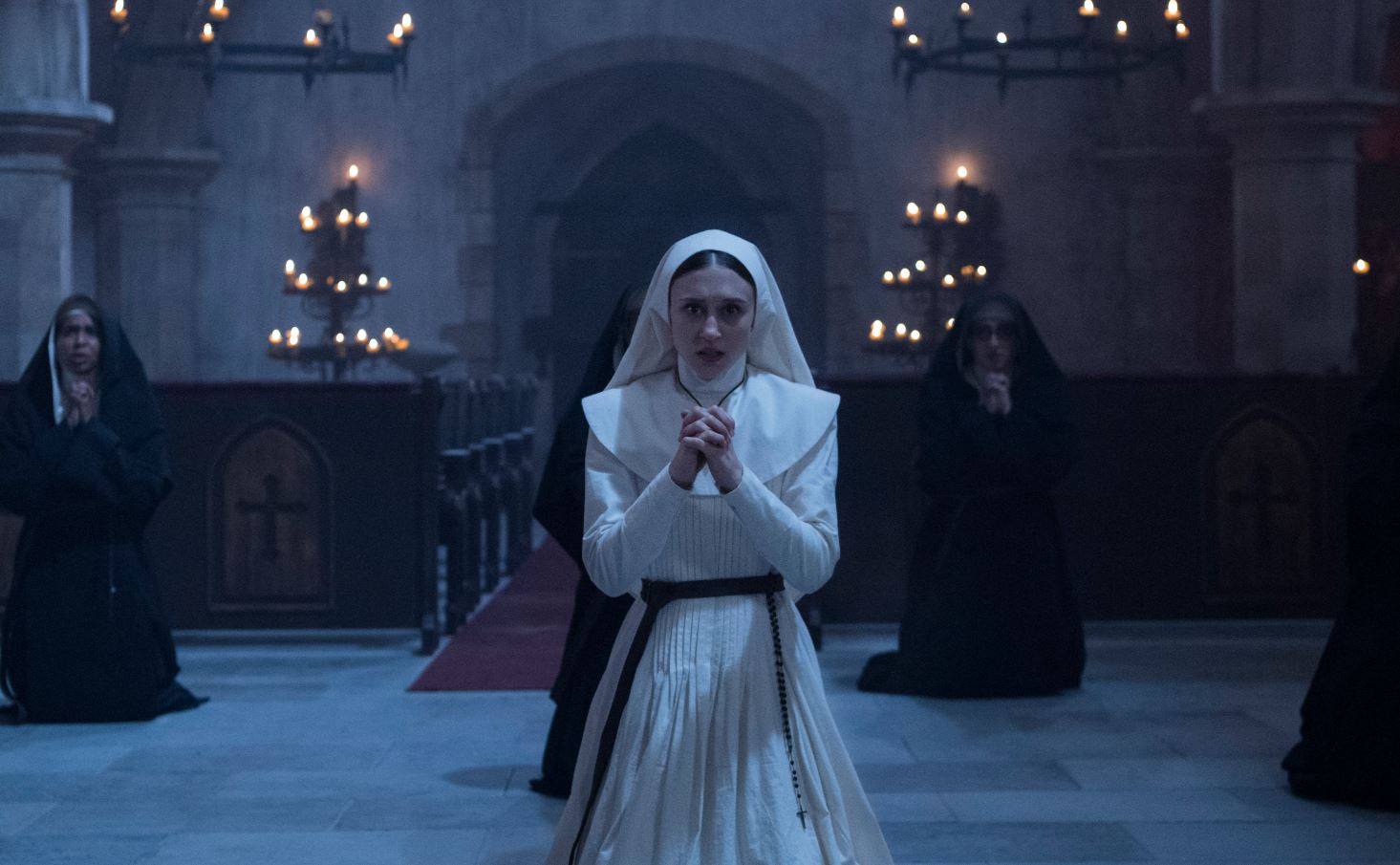 A young nun (Taissa Farmiga) kneeling in a church, praying.