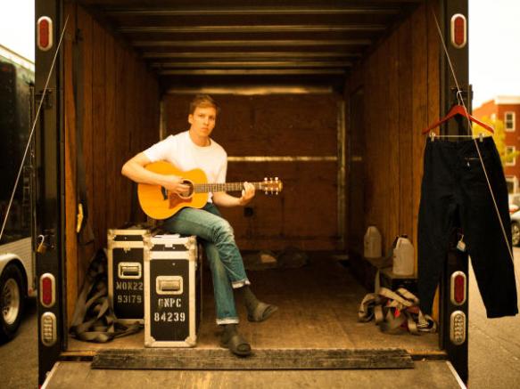 George Ezra sitting in an almost empty truck with a guitar in his lap.