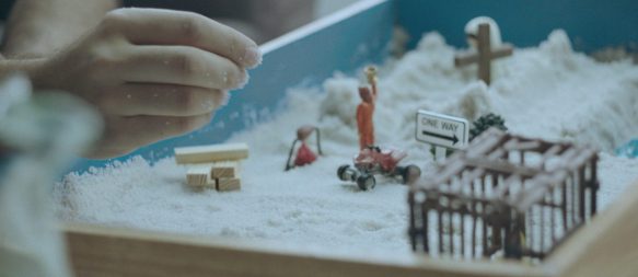 A sandbox with a child's hand that arranges tiny figures.