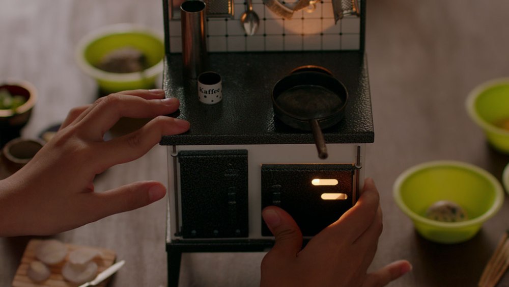 A doll stove with the hands of a girl using it.