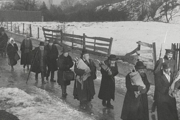 A line of people carrying bundles walks through the snow.
