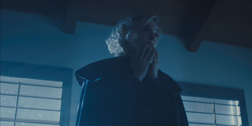 A woman dressed in black with her hands in front of her mouth. 