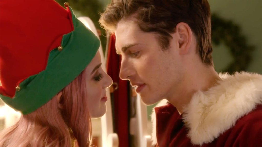 A young woman (Laura Marano) dressed as an elf and a young man (Gregg Sulkin) dresses as Santa Claus leaning in for a kiss. 