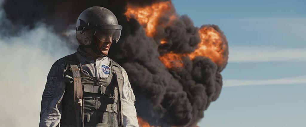 An astronaut (Ryan Gosling) in front of a column of smoke and flame. 