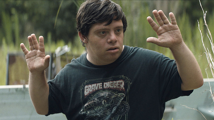 Zak (Zack Gottsagen) with his hands raised.