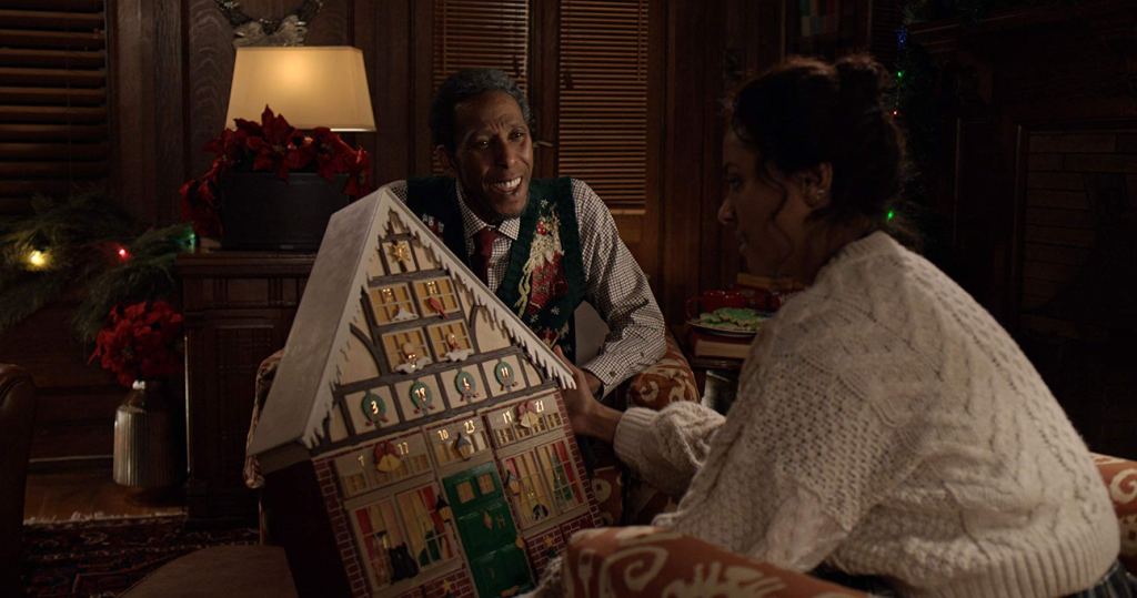 An old man (Ron Cephas Jones) giving a young woman (Kat Graham) an antique advent calendar shaped like a house.