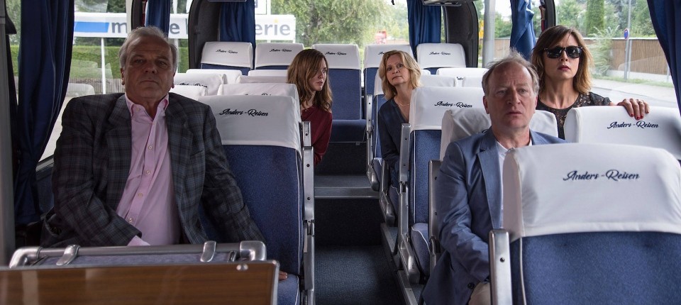 A bus with a five passengers all trying to see something at the front of the bus.