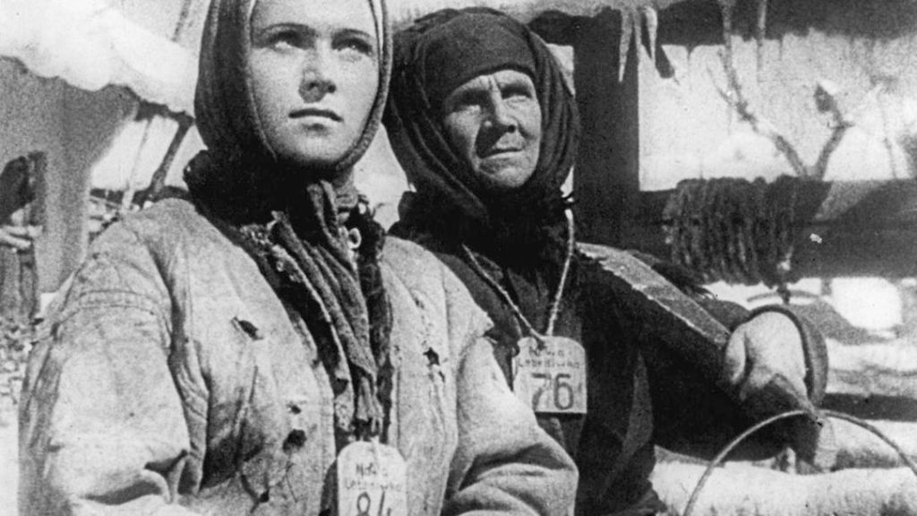 Two women with numbers hanging around their necks and tools in their hands.