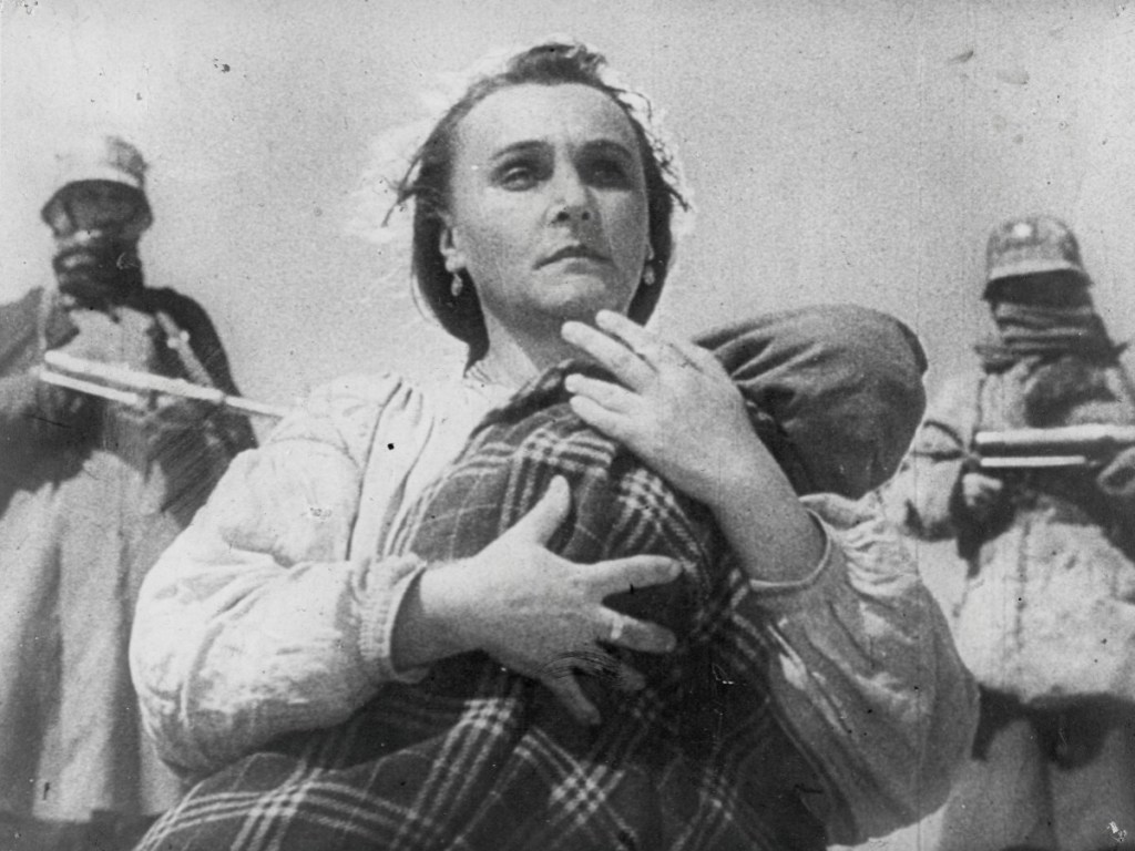 A woman clutching a baby, armed men standing behind her.