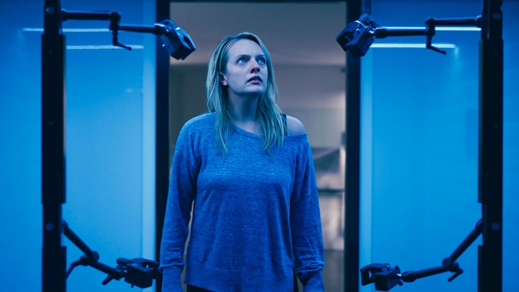 Cecilia (Elisabeth Moss) looking at some kind of machine. 
