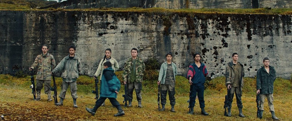 A group of teenagers standing in a military position in a line, being inspected.