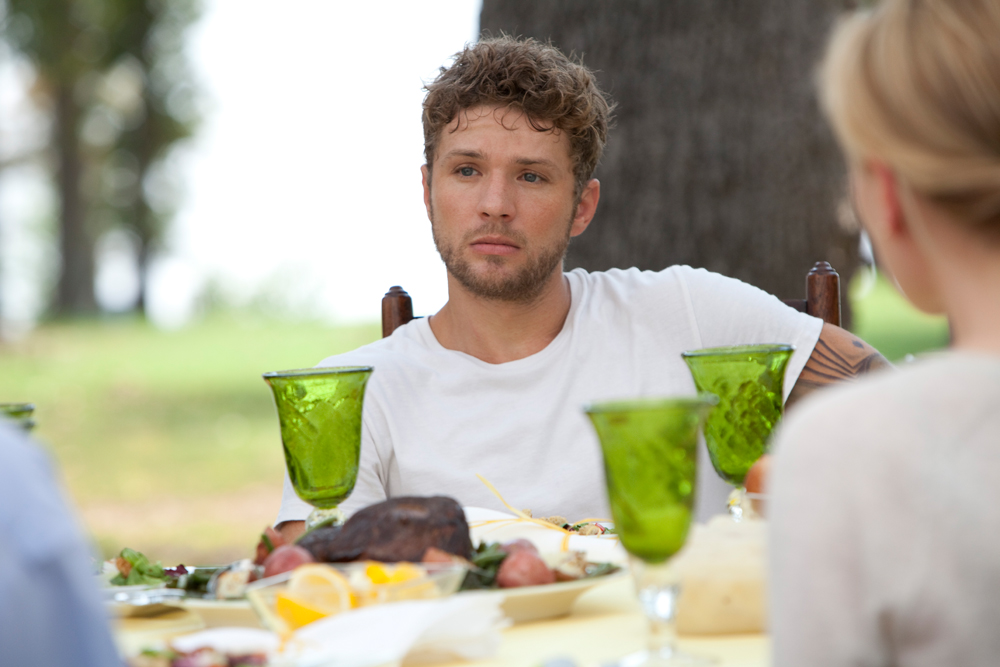 Scott (Ryan Philippe) sitting at a full table in the garden with a sad face.