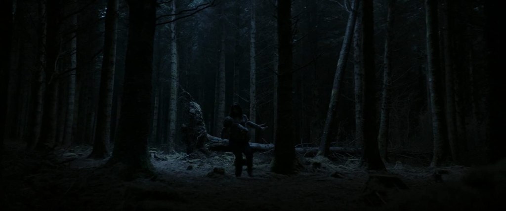 Sarah (Seána Kerslake) carrying Chris (James Quinn Markey) through the woods at night.