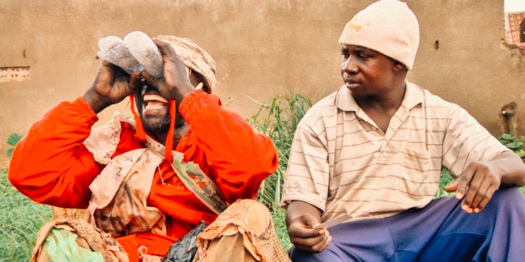 Two guys sitting in the street, one is using two plastic bottles as goggles.