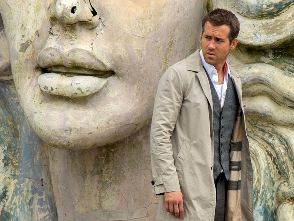 Damian (Ryan Reynolds) in front of the giant head of a statue.