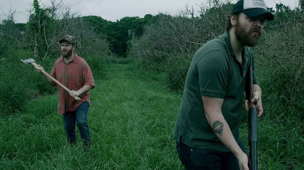 Wade (Henry Zebrowski) and Hank (Jeremy Gardner) stalking through a field. Wade as an axe, Hank a shotgun.