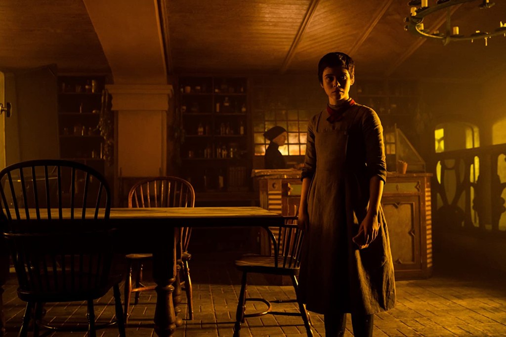 Gretel (Sophie Lillis) in the witch's cabin. The witch (Alice Krige) can be seen in the background.