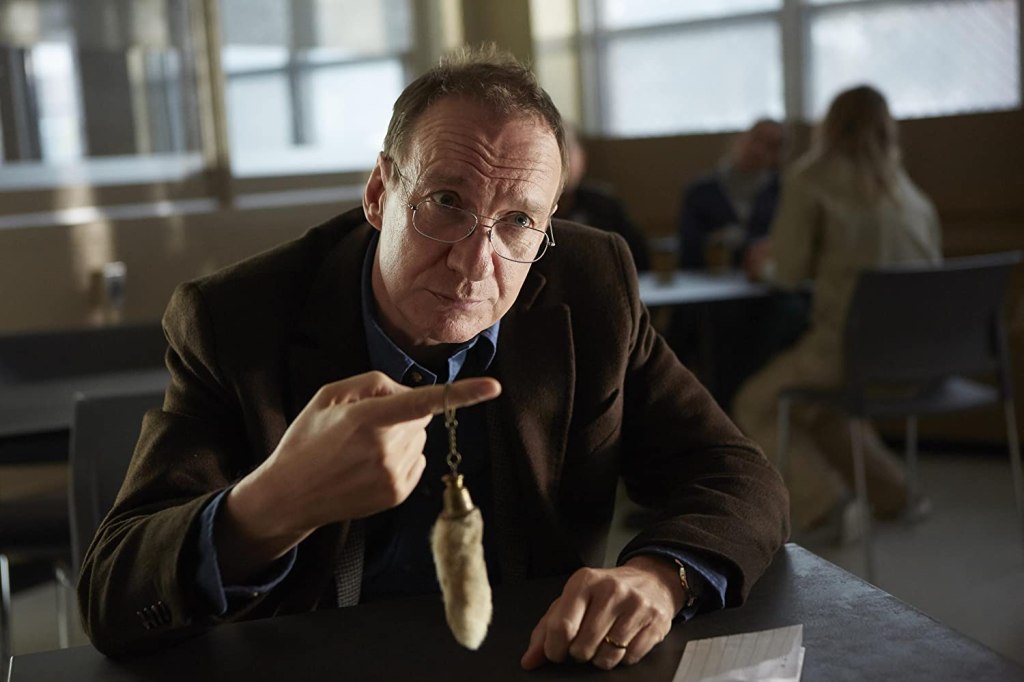 Jim (David Thewlis) holding out a rabbit's foot on a keychain. 