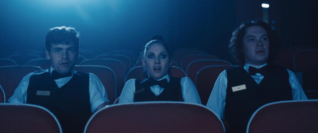 Abe (Evan Daves), Chaz (Jillian Mueller), and Ricky (Glenn Stott) watching a film together, looking shocked.