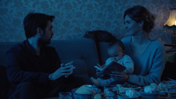 A man, a woman and a baby sitting on a couch. 