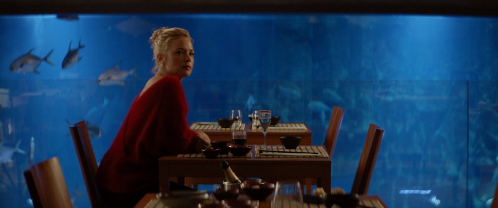 Sibyl (Virginie Efira) waiting in a restaurant, a giant aquarium behind her.