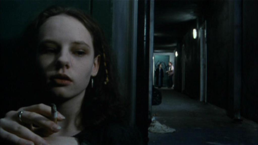 Lizzie (Heather Ann Foster) having a smoke in the hallway, listening to an argument.