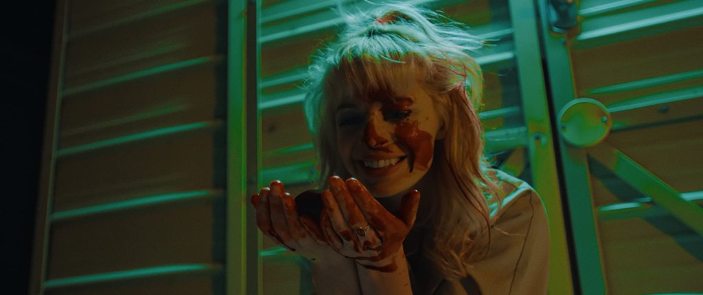 Regina (Chloe Farnworth) with blood all over her face and hands, cradling an organ and smiling at it.