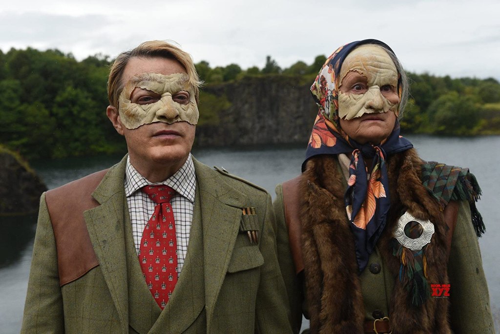 The Duke (Eddie Izzard) and the Duchess (Georgie Glen) in strange masks. 