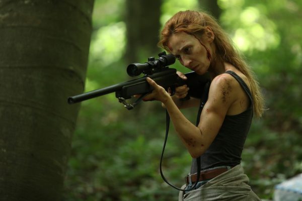 Ayse (Billur Melis Koç) with a rifle in the woods.