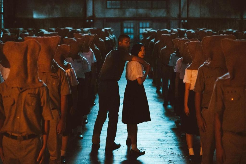 Wei (Jing-Hua Tseng) and Fang (Gingle Wang) making their way through students standing in military order, all with bags over their heads.