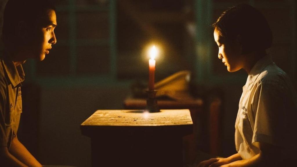 Wei (Jing-Hua Tseng) and Fang (Gingle Wang) sitting at a desk, a candle between them. 