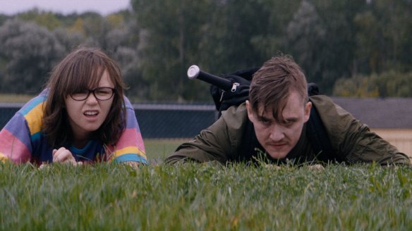 Simon (Kyle Gallner) and Patty (Emily Skeggs) lying in the grass, observing something.
