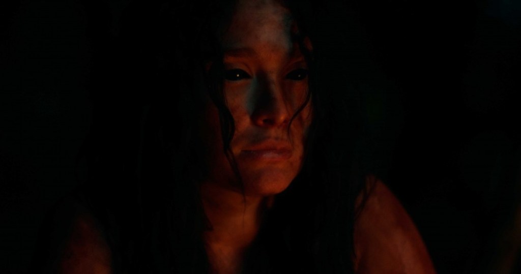 Kerana (Lali Gonzalez) with all-black eyes lit by campfire.