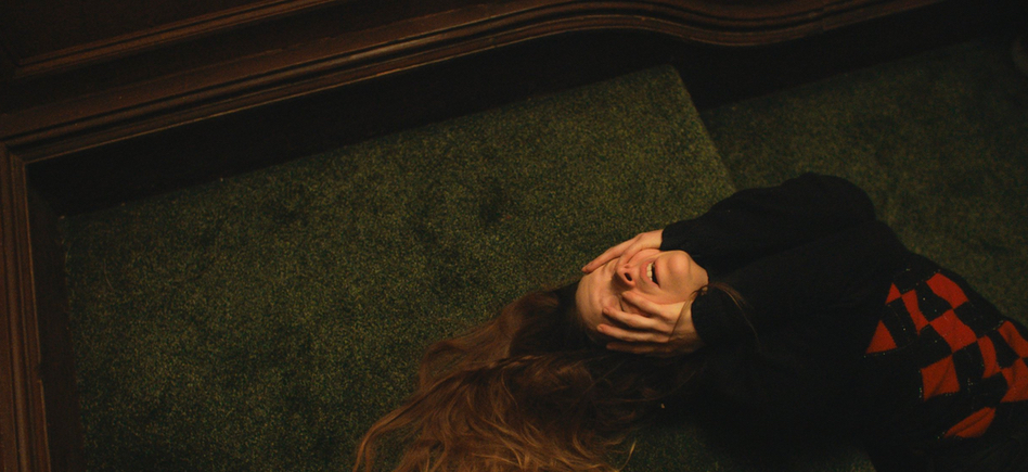 Maud (Morfydd Clark) lying on the stairs, covering her face with her hands.