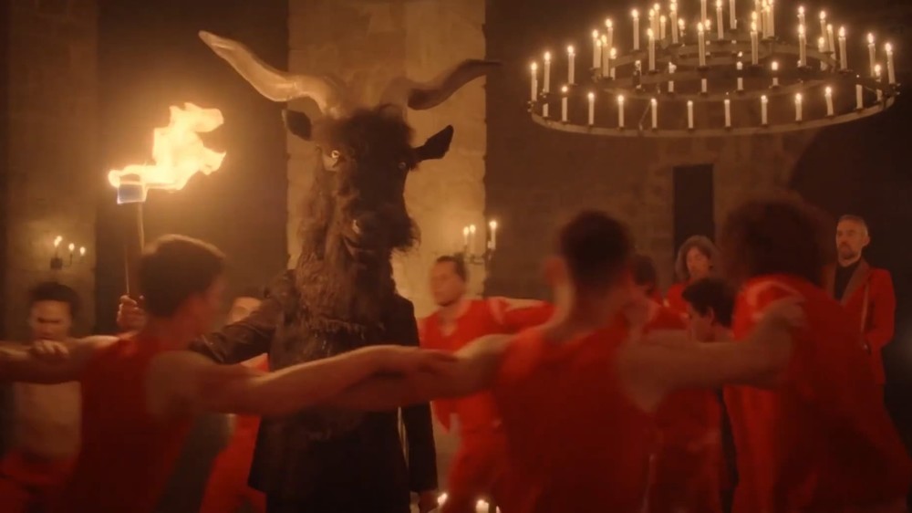 A group of devils dressed in red, dancing around a goat-headed man.