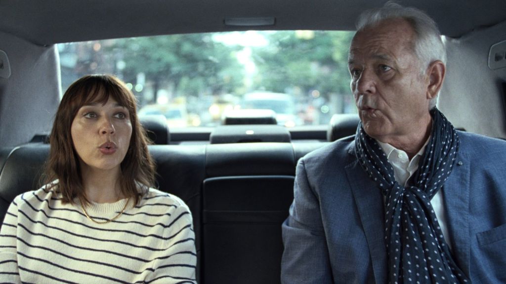 Laura (Rashida Jones) and Felix (Bill Murray) in the back of a car, both whistling.