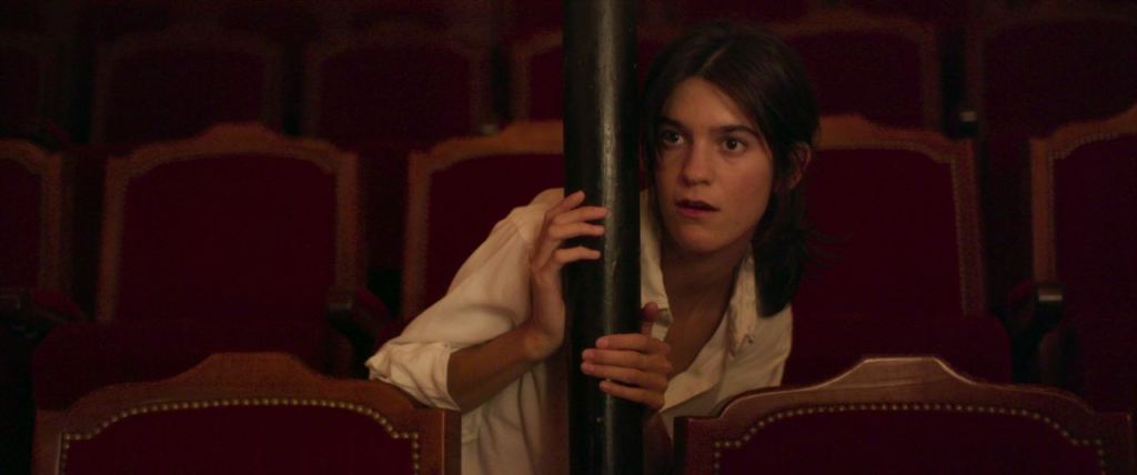 Suzanne (Suzanne Lindon) hiding in the audience area of the theater.