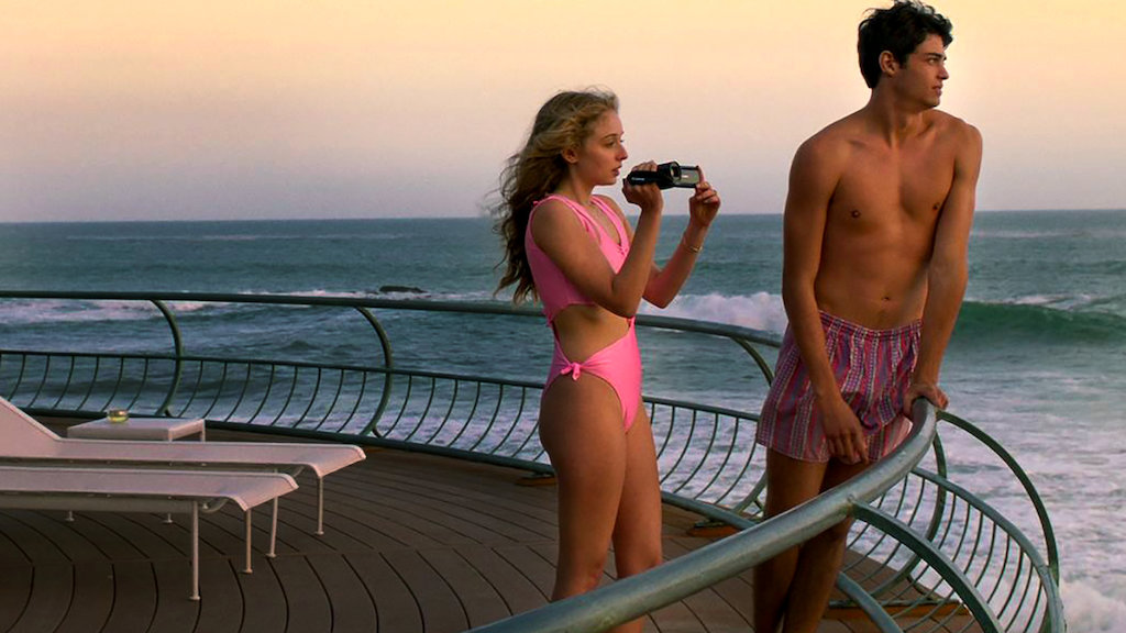 Penny (Carson Meyer) and Johnny (Noah Centineo) standing on a balcony over the sea. 