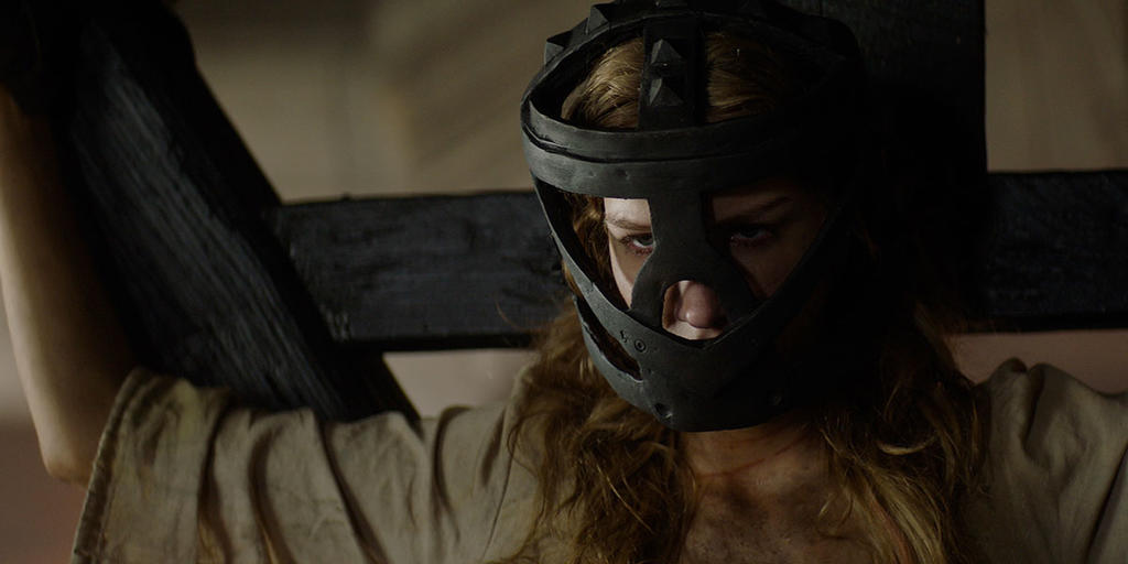 Grace (Charlotte Kirk) bound to a cross, with an iron mask that muzzles her.