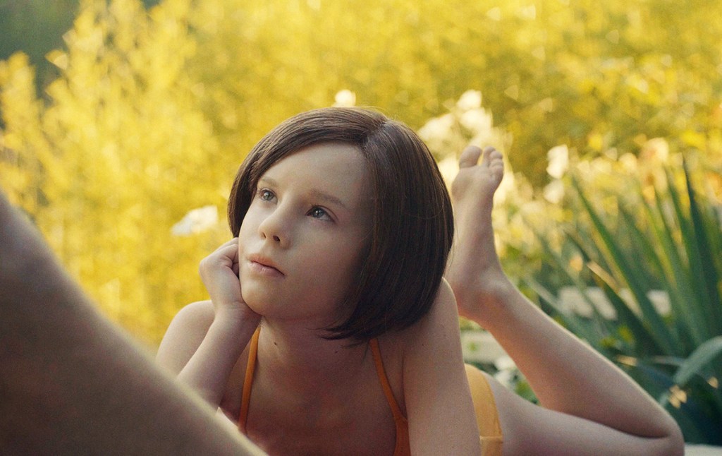 Ellie (Lena Watson) lying in the grass in a bathing suit.