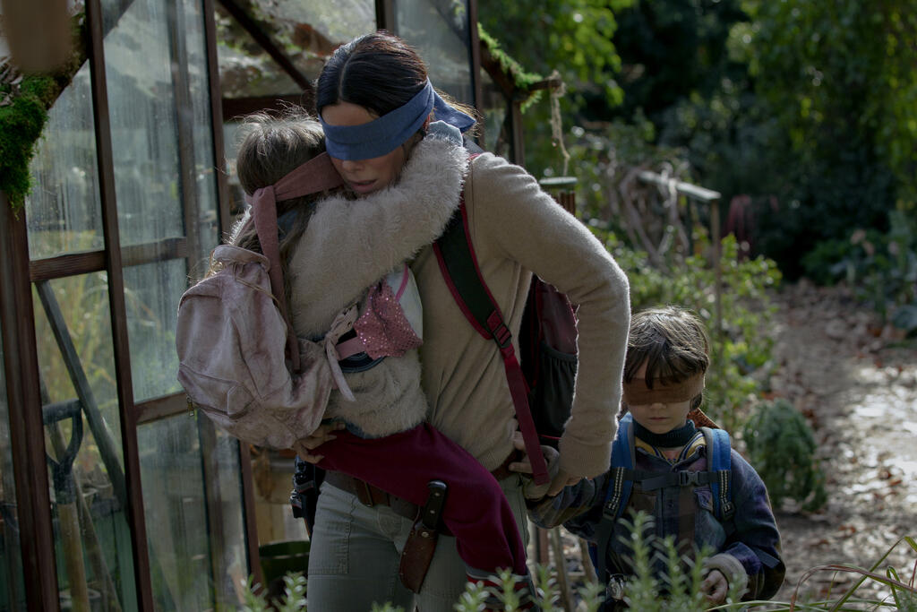 Blindfolded, Malorie (Sandra Bullock) carries her daughter Girl (Vivien Lyra Blair) and holds her son Boy's (Julian Edwards) hand. The children are blindfolded as well.