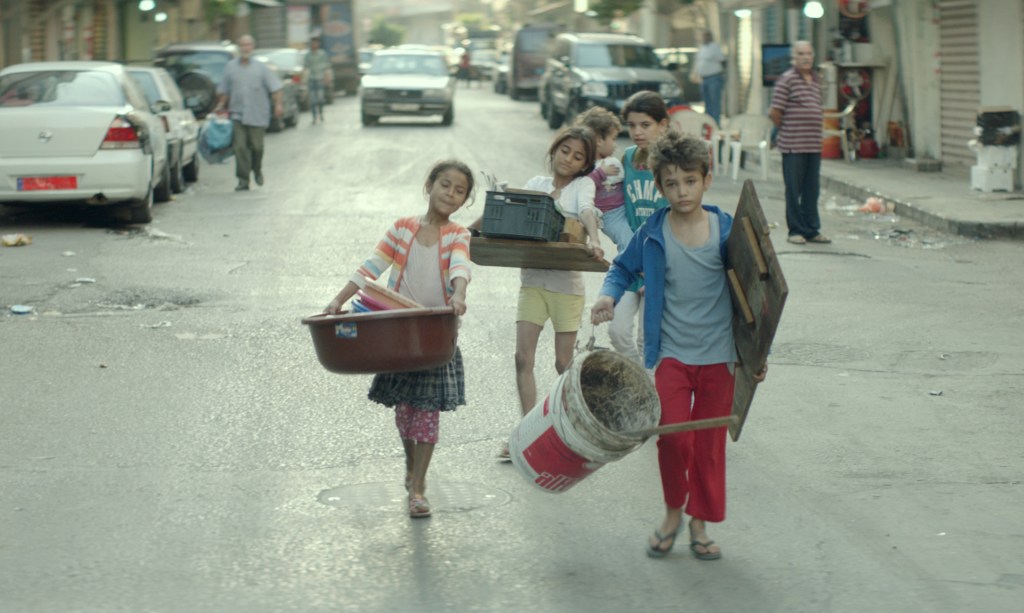 Zain (Zain Al Rafeea) leading a group of children, all carrying building supplies.