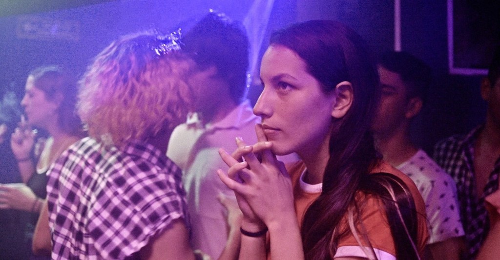 Iris (Sofia Cabrera) in a club, watching something. 