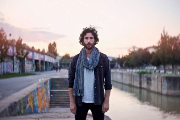 A single guy in a scarf standing next to the danube in the sunset.
