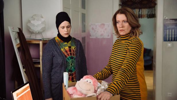 Wanda (Caroline Peters) collecting her daughters' toys as Nina (Chantal Zitzenbacher) looks on.