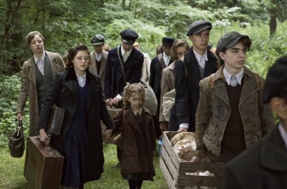 Betty (Sophie Stockinger) leading a little girl in a group of children making their way through a forest.