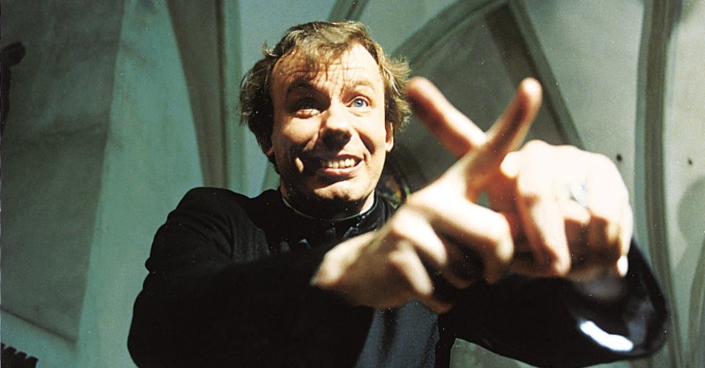 Helden's priest (Ludger Pistor) making a cross with his fingers.